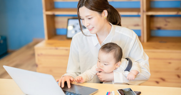 子どもを抱えながらテレワークをする女性